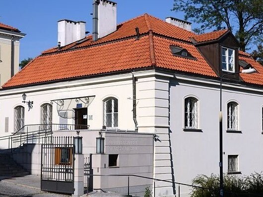 Zdjęcie przedstawia kamienicę z czerwoną dachówką i białej elewacji, w której mieści się stołówka Uniwersytetu Warszawskiego