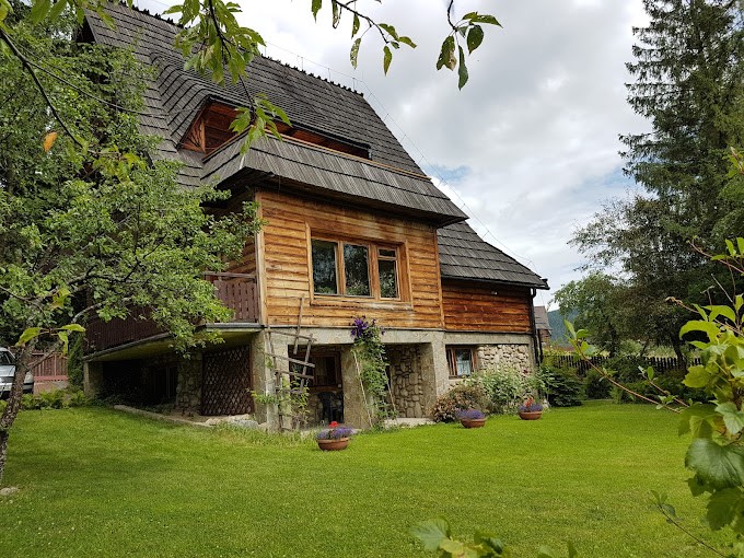 Zdjęcie przedstawia drewniany Dom Pracy Twórczej i Wypoczynku "Szeligówka" od południowej strony ogrodu w otoczeniu zielonej trawy oraz drzew.