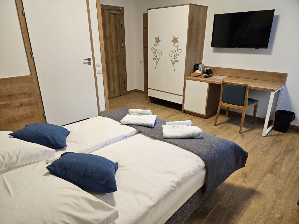 Zdjęcie przedstawia pokój nr 01 dla osób z niepełnosprawnościami: przodu łóżko w głębi z lewej drzwi do łazienki oraz szafa z biurkiem