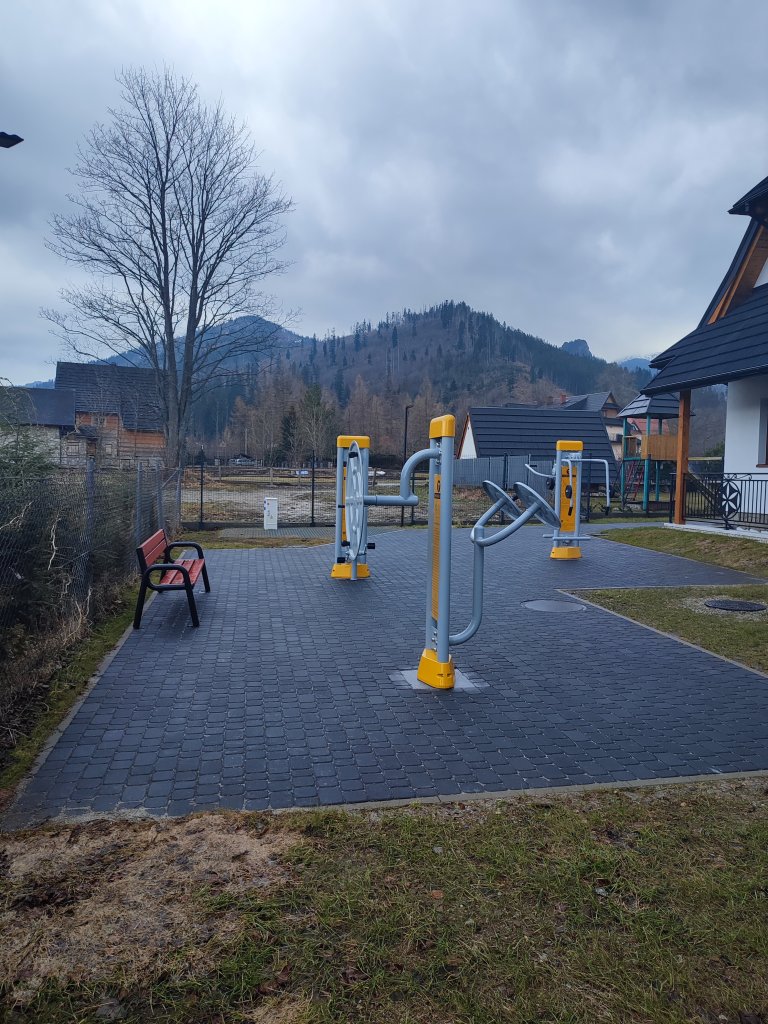 Three outdoor gym stations with bench on the left and building on the right.